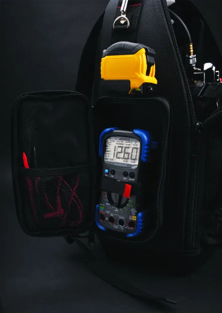 The left side pocket open, holding a digital multimeter reading 126.0, with a mesh pocket of test leads on the flap.
