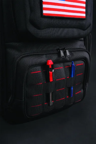 Elastic webbing on the front of the bag holding a red marker and a blue pen, below a US flag patch.