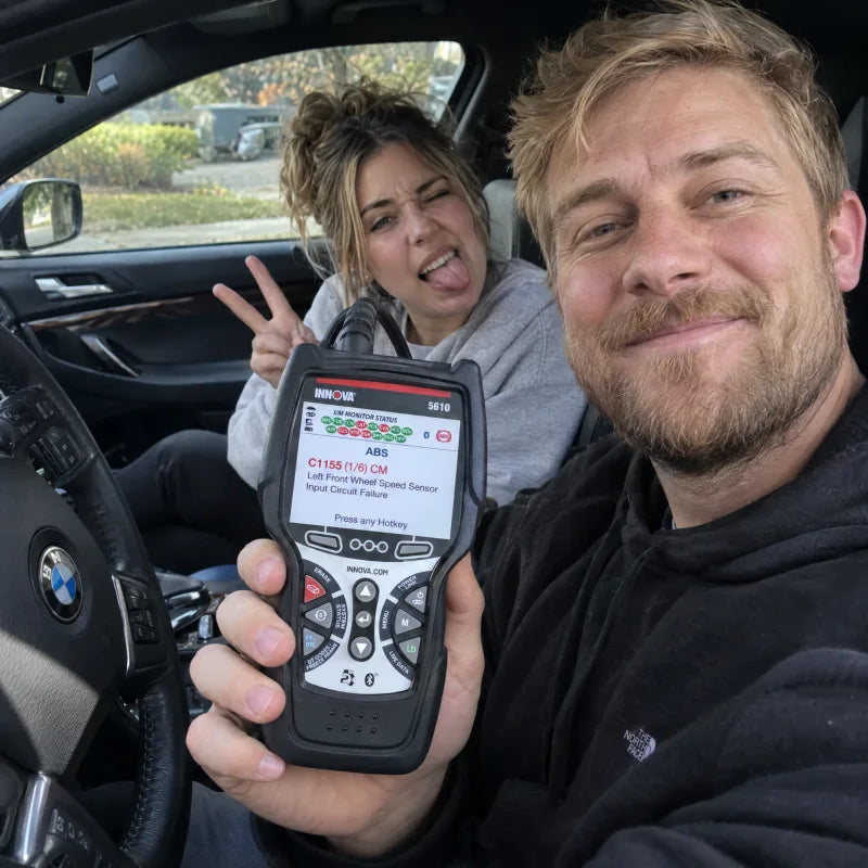 Two people in a car, one holding an Innova 5610 showing an ABS fault